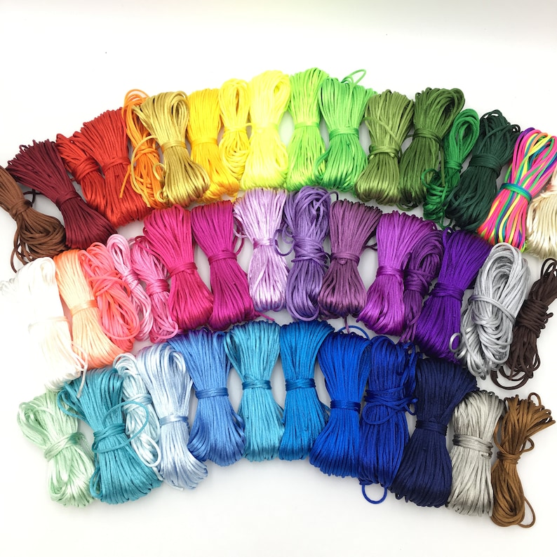 May include: A collection of colorful satin cords in a rainbow of hues. Bundles of cord are arranged in shades of red, orange, yellow, green, blue, purple, and brown. The cords are tightly wound and tied, ready for crafting projects.