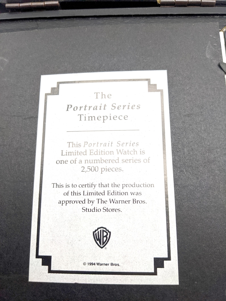 Pu&ograve; includere: Una carta bianca con testo nero, con la scritta "The Portrait Series Timepiece". La carta descrive un orologio in edizione limitata di 2.500 pezzi, approvato da The Warner Bros. Studio Stores. Il logo Warner Bros. &egrave; visibile.