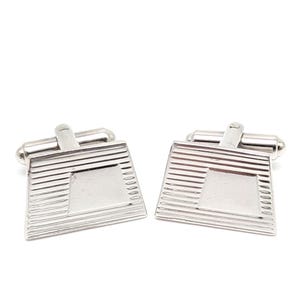 May include: A pair of silver cufflinks. Each cufflink has a rectangular shape with a square center and horizontal lines. The cufflinks have a shiny, metallic finish and a hinged bar for securing them to a shirt cuff.