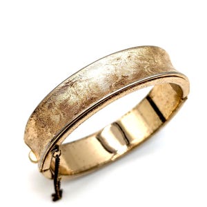 Pulsera rígida articulada con diseño de espiral en tono dorado cepillado de Sarah Coventry con cadena de seguridad