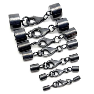 Op de afbeelding: Verschillende gunmetal-kleurige magnetische sluitingen voor het maken van sieraden. Elke sluiting heeft een cilindrisch eindstuk dat via een kleine ketting is verbonden met een karabijnhaak. De sluitingen zijn geplaatst op een witte achtergrond.