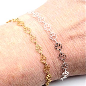 May include: Two delicate bracelets featuring paw print charms. One bracelet is gold-toned, the other is silver-toned. The paw print charms are linked together, creating a stylish and pet-themed accessory.