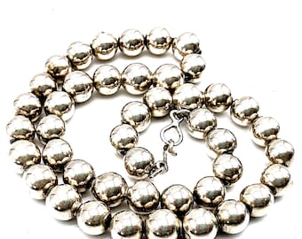 May include: A necklace composed of numerous polished silver-toned spherical beads arranged in a circular pattern. The beads have a reflective, metallic surface and are connected by a silver-toned metal hook-and-eye clasp mechanism.