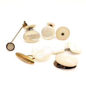 May include: A collection of assorted cufflinks featuring iridescent white mother-of-pearl faces in oval, round, and rectangular shapes. The set includes various metal backings in gold and silver tones, with one long, thin metal bar attachment.