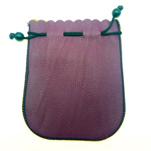 Può includere: Un piccolo astuccio in pelle viola con chiusura a coulisse. L'astuccio ha un bordo superiore smerlato ed è rifinito con cuciture verde scuro. Il cordino è verde scuro e ha una perla di legno su ciascuna estremità. L'astuccio è alto circa 13 cm.