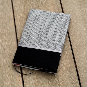 Könnte beinhalten: Ein grauer und schwarzer Notizbuchumschlag mit einem weißen geometrischen Muster. Der Umschlag hat einen schwarzen Streifen am unteren Rand.