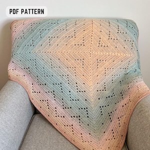 Puede incluir: Una manta de ganchillo en colores pastel rosa, melocotón y azul, sobre un sillón gris. La manta presenta un diseño geométrico calado. El texto "PDF PATTERN" está en la esquina superior izquierda.