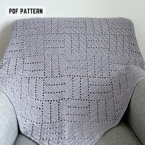 May include: A light gray crocheted blanket with a geometric pattern, draped over a gray armchair. The blanket features a repeating square design with open spaces. The words "PDF PATTERN" are in a white box in the upper left corner.