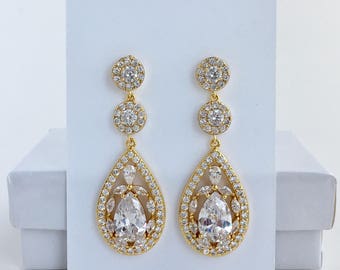 May include: Gold teardrop earrings featuring a large pear-shaped crystal surrounded by smaller crystals. The earrings have three round crystal accents.