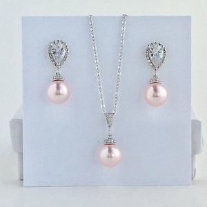 May include: A delicate bridal necklace and earrings set featuring a pear-shaped crystal with a halo of smaller crystals and a pink pearl pendant.