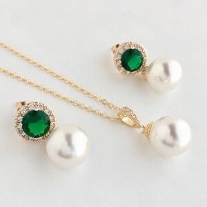 Puede incluir: Un conjunto de collar y pendientes de oro con una piedra preciosa verde rodeada de diamantes de imitaci&oacute;n transparentes y un colgante de perla blanca.