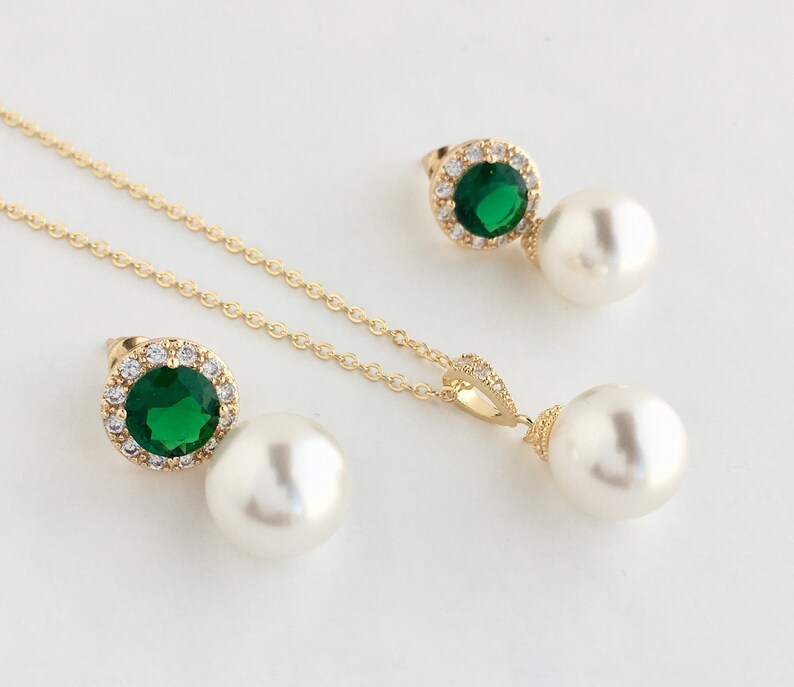 Puede incluir: Un conjunto de collar y pendientes de oro con una piedra preciosa verde rodeada de diamantes de imitaci&oacute;n transparentes y un colgante de perla blanca.