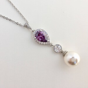 May include: A silver necklace with a pear-shaped purple gemstone surrounded by clear stones and a single pearl pendant.