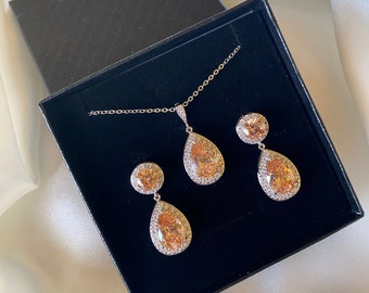 May include: A set of pear-shaped earrings and a necklace with a matching pendant. The jewelry features clear stones with a champagne-colored center.