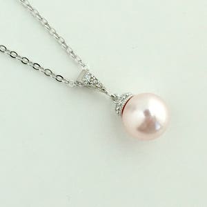 May include: A silver chain necklace with a delicate pendant featuring a single, large, blush-coloured pearl accented with small, clear cubic zirconia stones.