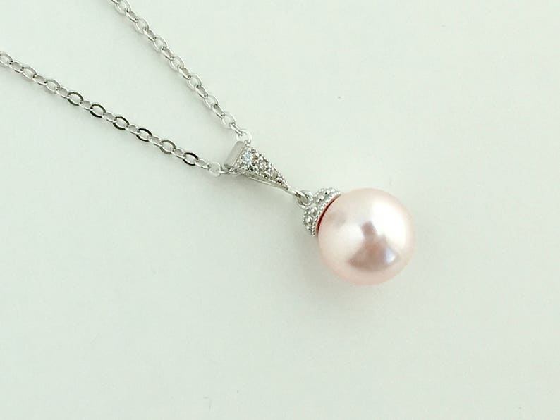 May include: A silver chain necklace with a delicate pendant featuring a single, large, blush-coloured pearl accented with small, clear cubic zirconia stones.