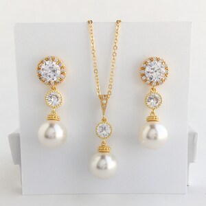 May include: A gold necklace and earrings set with a large round crystal pendant and matching earrings. The pendant and earrings are accented with smaller crystals and a pearl drop.