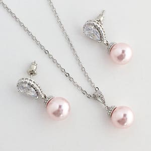 May include: A silver necklace and earrings set with a teardrop-shaped crystal and a pink pearl pendant.