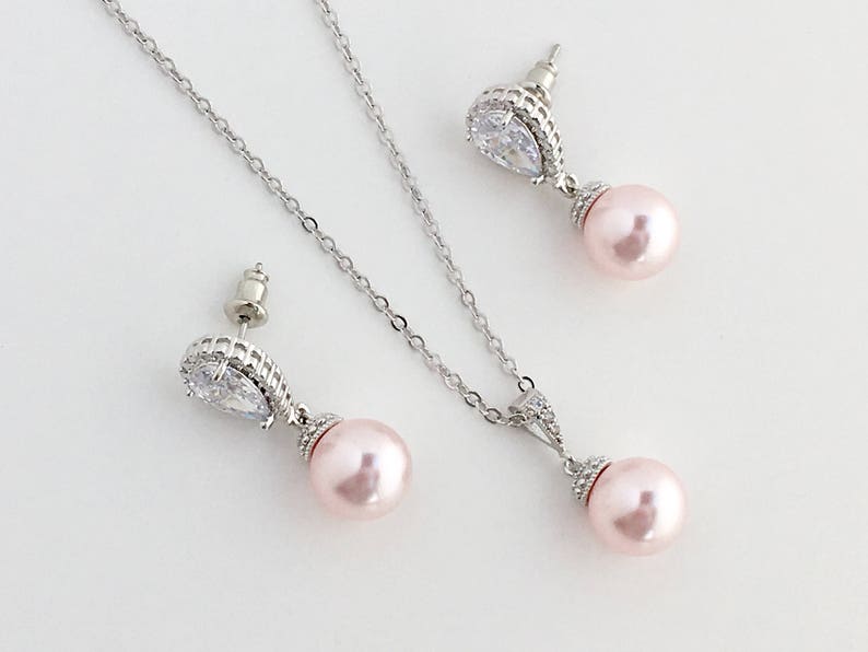May include: A silver necklace and earrings set with a teardrop-shaped crystal and a pink pearl pendant.