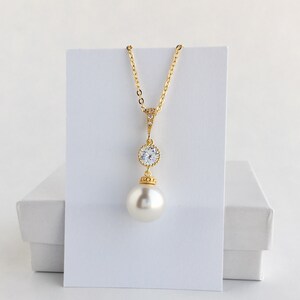 May include: A gold necklace with a large pearl pendant and a smaller crystal pendant. The necklace is on a white background.