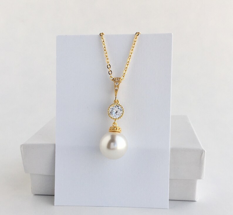 May include: A gold necklace with a large pearl pendant and a smaller crystal pendant. The necklace is on a white background.