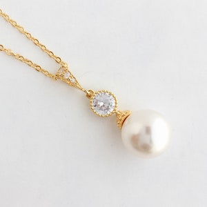 May include: A gold necklace with a delicate chain and a pendant featuring a sparkling clear crystal and a large white pearl.