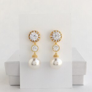 May include: Gold tone earrings with a large clear crystal surrounded by smaller crystals, a smaller clear crystal, and a large faux pearl.