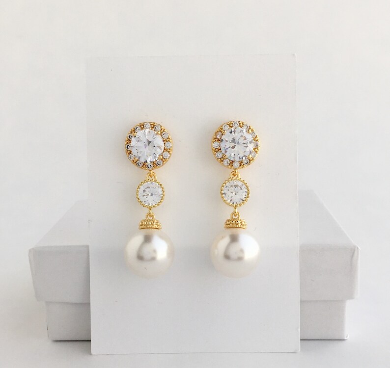 May include: Gold tone earrings with a large clear crystal surrounded by smaller crystals, a smaller clear crystal, and a large faux pearl.
