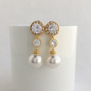 May include: Gold tone earrings with a large round clear crystal surrounded by smaller crystals, a smaller round clear crystal, and a pearl drop.