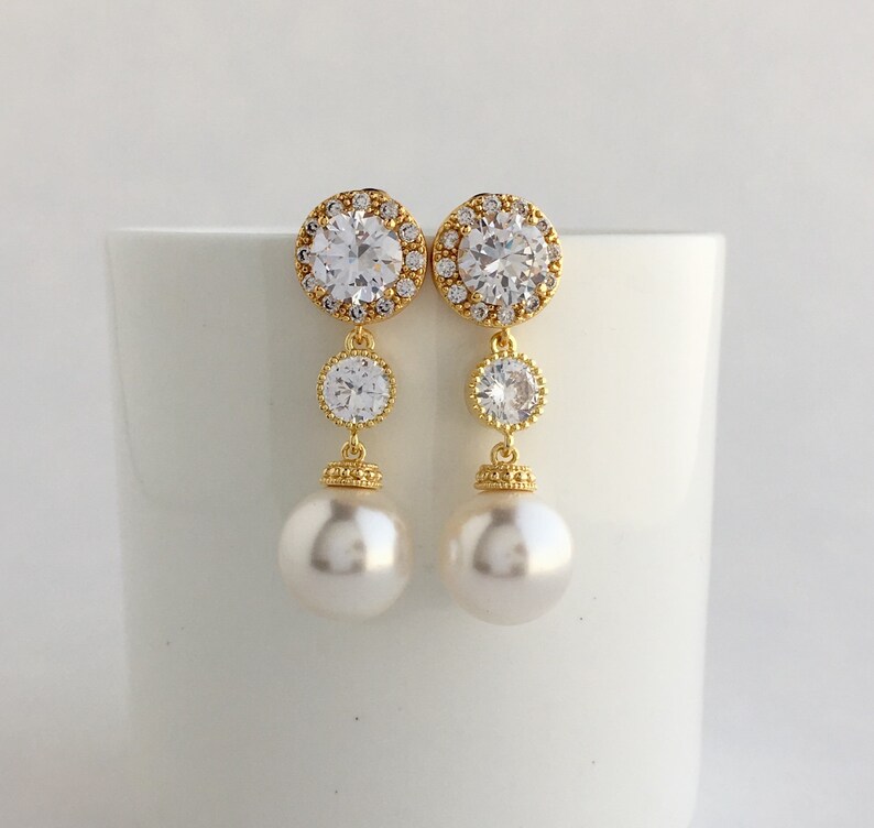 May include: Gold tone earrings with a large round clear crystal surrounded by smaller crystals, a smaller round clear crystal, and a pearl drop.