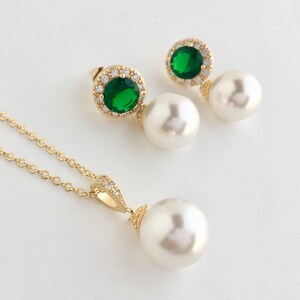 Puede incluir: Un conjunto de collar y pendientes de oro con un gran colgante de perla blanca y pendientes a juego. Los pendientes presentan una piedra preciosa verde rodeada de piedras transparentes m&aacute;s peque&ntilde;as.