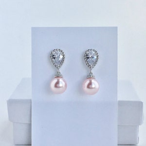 May include: A pair of silver earrings with a teardrop-shaped crystal and a pink pearl dangling from each earring.