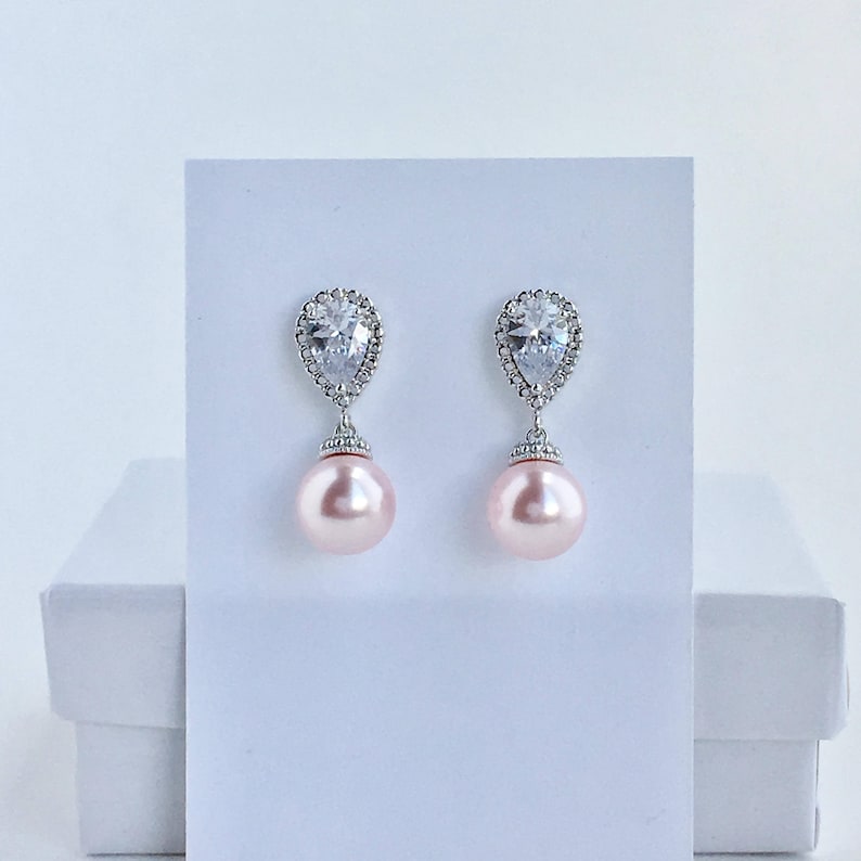 May include: A pair of silver earrings with a teardrop-shaped crystal and a pink pearl dangling from each earring.