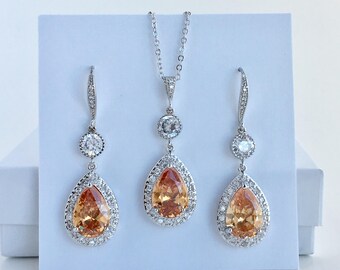 May include: A bridal jewelry set with a pear-shaped pendant necklace and matching earrings. The set features a large, teardrop-shaped orange gemstone surrounded by smaller clear stones.