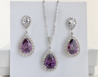 Könnte beinhalten: Ein silbernes Halsketten- und Ohrring-Set mit einem birnenförmigen violetten Edelstein, der von einem Heiligenschein aus kleineren klaren Steinen umgeben ist.