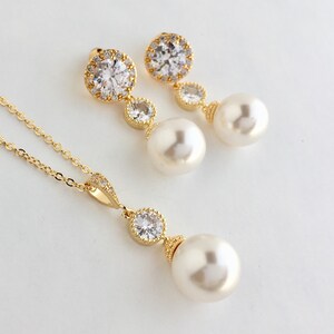 May include: A gold necklace and earrings set with a pearl and crystal pendant. The necklace has a delicate chain and the earrings have a small crystal drop.