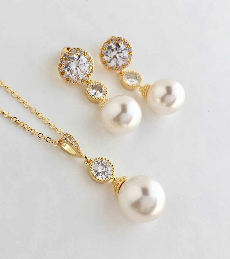 May include: A gold necklace and earrings set with a pearl and crystal pendant. The necklace has a delicate chain and the earrings have a small crystal drop.