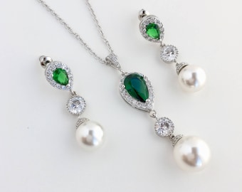 May include: A silver necklace and earrings set with a pear-shaped green gemstone surrounded by clear rhinestones and a pearl drop.