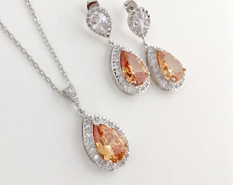May include: A silver necklace and earrings set with pear-shaped orange gemstones surrounded by smaller clear stones.