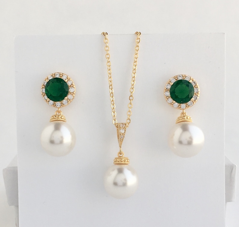 Puede incluir: Un collar y pendientes de oro con una gran piedra preciosa verde rodeada de piedras m&aacute;s peque&ntilde;as transparentes y una perla colgante.