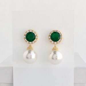 Puede incluir: Pendientes de oro con una piedra esmeralda verde rodeada de diamantes de imitaci&oacute;n transparentes y una perla blanca.