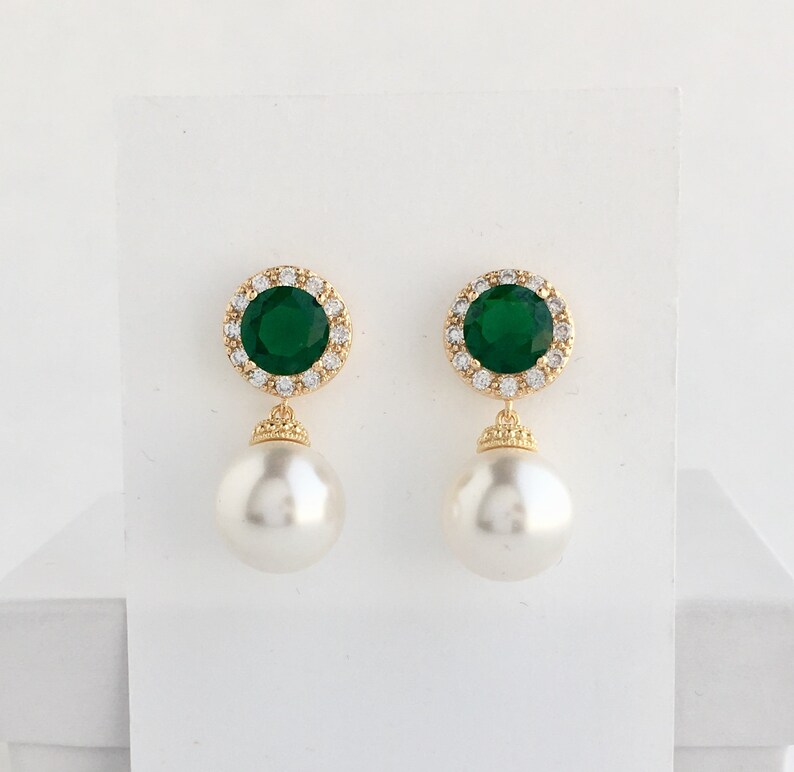 Puede incluir: Pendientes de oro con una piedra esmeralda verde rodeada de diamantes de imitaci&oacute;n transparentes y una perla blanca.