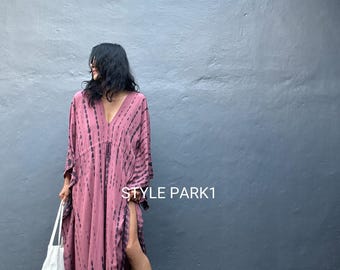 May include: A long, flowing, mauve dress with black tie-dye stripes. The dress has a deep V-neck and a high slit on one side. A white tote bag is held in one hand. The text "STYLE PARK1" is visible on the right side of the image.