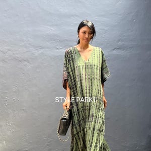 Peut inclure: Une femme portant une robe maxi en tie-dye vert et noir avec un sac à main noir. La robe a un col en V et des manches courtes. Le texte "STYLE PARK1" est visible sur la robe.