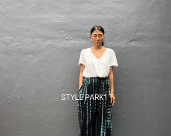 Könnte beinhalten: Eine Person trägt ein weißes V-Ausschnitt-T-Shirt und eine Hose mit weitem Bein. Die Hose ist schwarz mit vertikalen blau-weißen Batikstreifen. Der Text "STYLE PARK1" ist auf der Hose zu sehen.