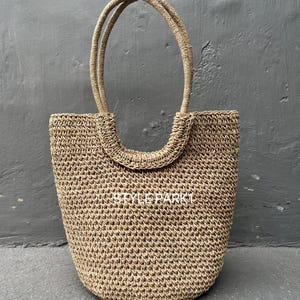 Pu&ograve; includere: Una grande borsa tote beige intrecciata con due manici spessi e arrotondati. La borsa &egrave; realizzata in un materiale intrecciato fitto, che le conferisce un aspetto testurizzato.