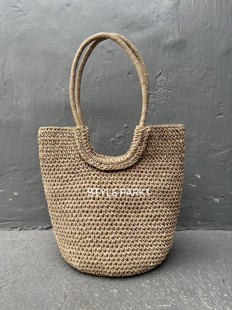 Pu&ograve; includere: Una grande borsa tote beige intrecciata con due manici spessi e arrotondati. La borsa &egrave; realizzata in un materiale intrecciato fitto, che le conferisce un aspetto testurizzato.