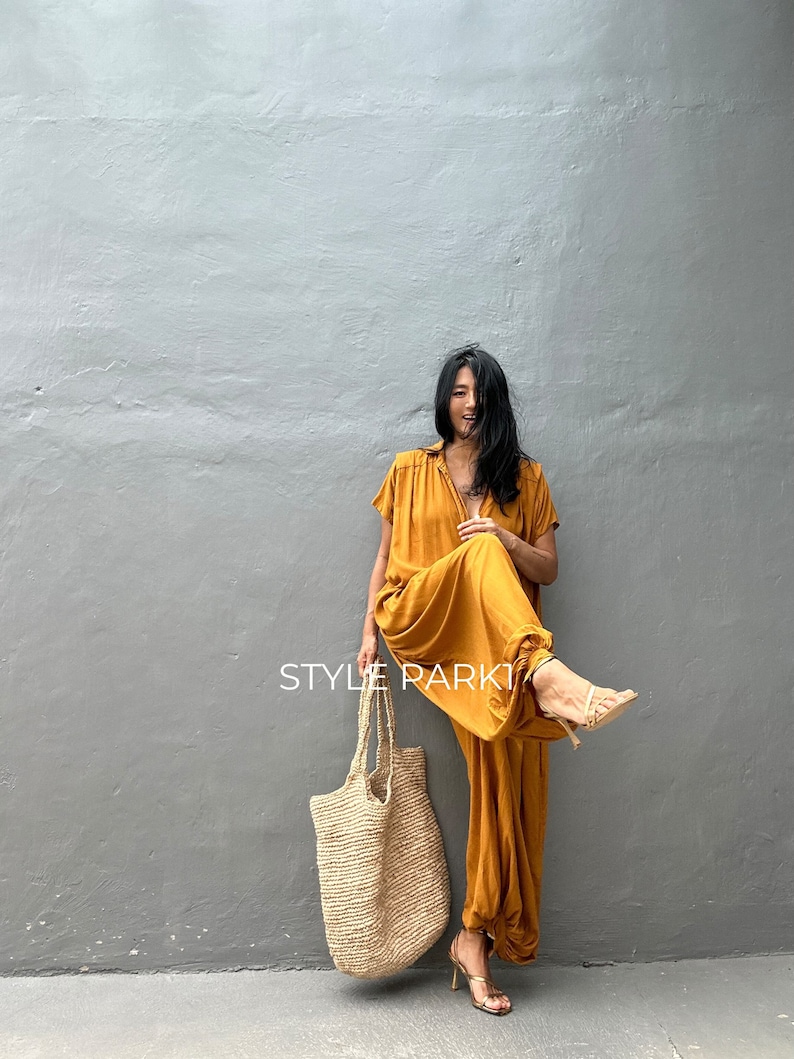 May include: A woman wearing a mustard yellow jumpsuit with a gathered hem and short sleeves. She is holding a large, natural fiber tote bag and smiling. The text "STYLE PARK" is visible in the image.