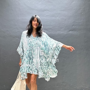 May include: A short, flowing dress with a V-neck and a distinctive teal and white animal print. The dress features ruffled edges and is worn with a cream-coloured tote bag. This dress is a stylish and comfortable garment.