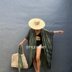 May include: A woman wearing a green and black tie-dye kimono with a straw hat and a black bikini bottom. She is holding a large woven tote bag with a green and black tie-dye ribbon. The text "STYLE PARK1" is visible in the image.